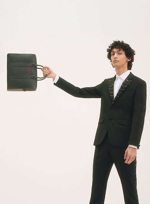 A man in a Givenchy suit and Louboutin bag
