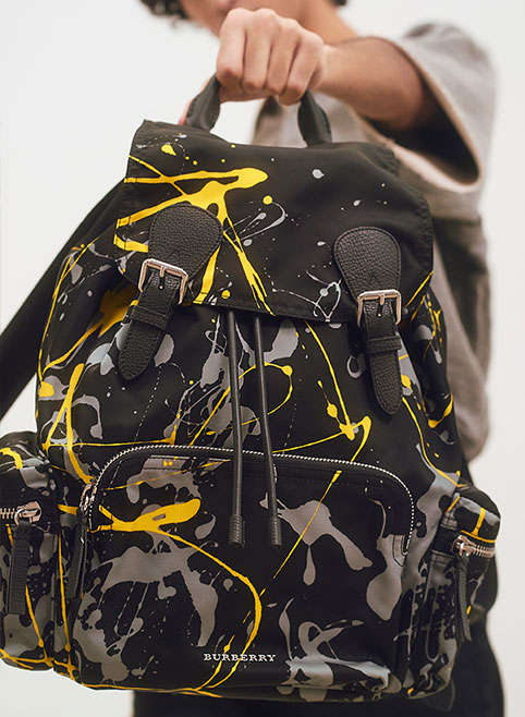 A man holding a paint-splattered Burberry backpack