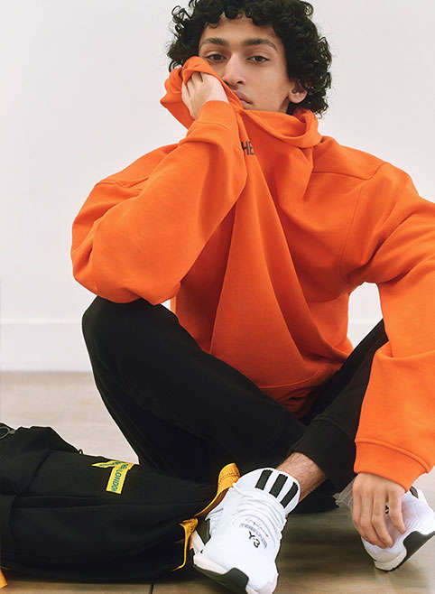 A man sitting down in an orange hoody and jogging bottoms